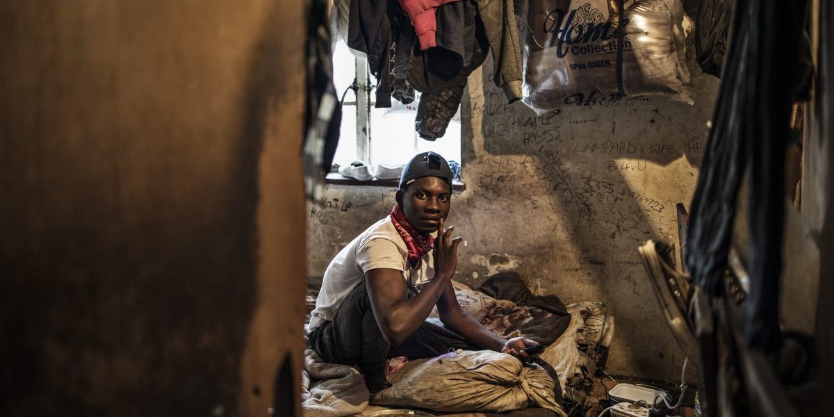 A foreign migrant sits on his bed inside a boarded up room occupied by two people on the upstairs floor in a building in the Kwa Mai Mai area in Johannesburg. Image: Getty, Marco Longari/AFP