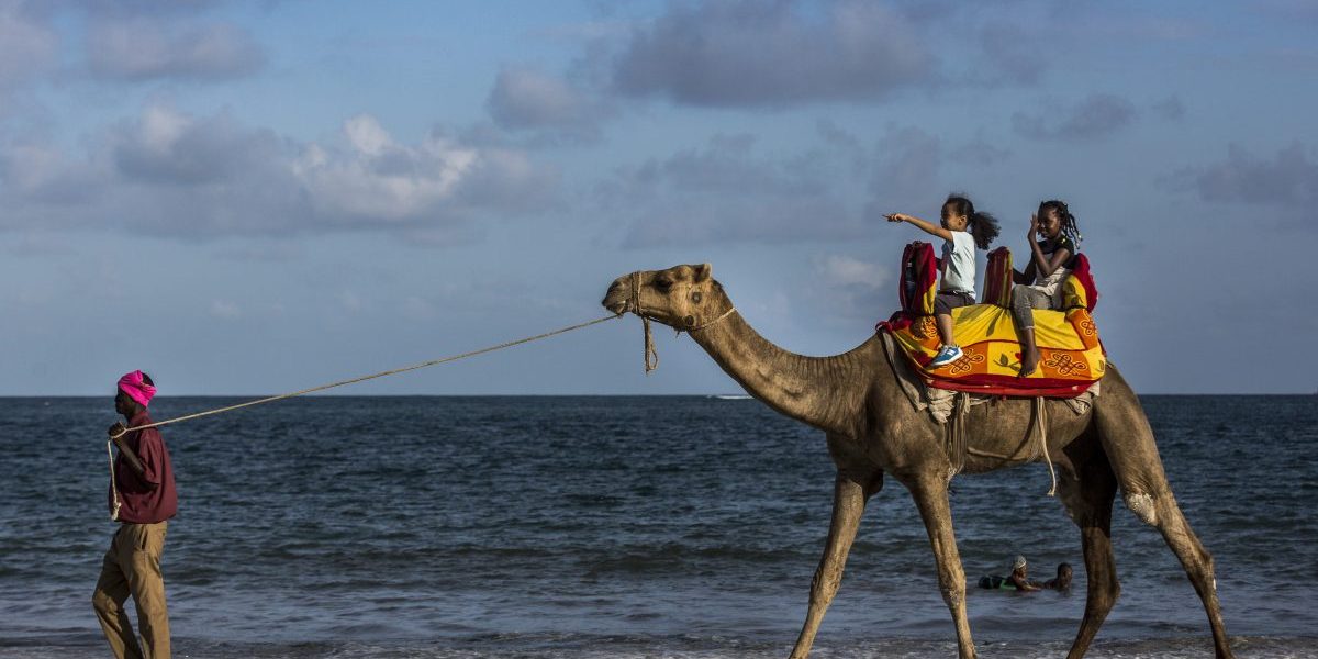 A vendor leads a camel carrying two children along the beachfront in Mombasa, Kenya. Image: Getty, Luis Tato/Bloomberg,
