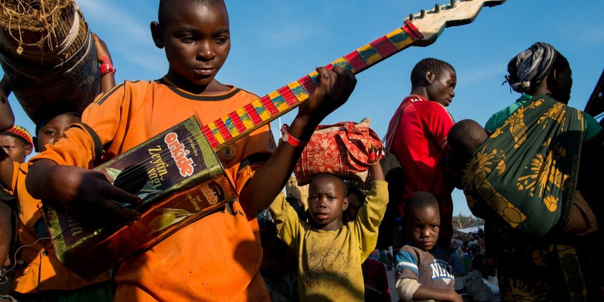 Burundian refugee Richard Samuel, 14, plays his home made guitar as he waits to be transferred to Nyarugusu Refugee Camp from Lake Tanganyika Stadium in Kigoma. Image: Getty, Daniel Hayduk/AFP