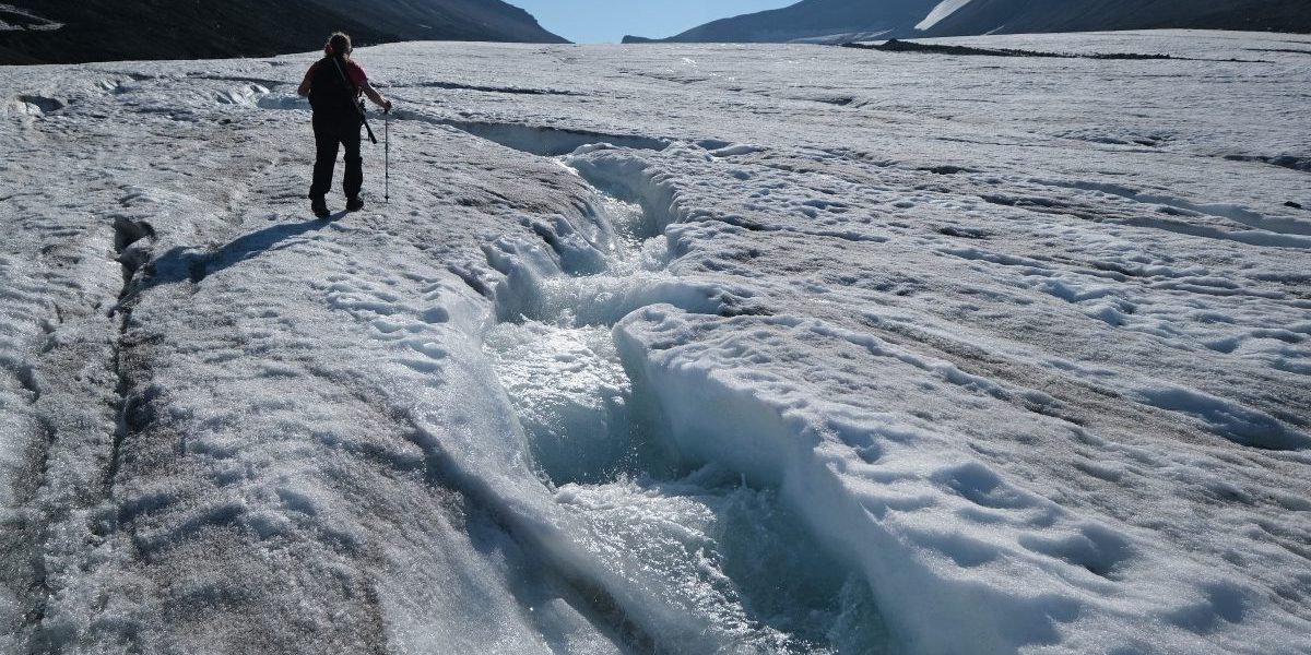 A guide walks along a winding channel carved by rushing water on the surface of the melting Longyearbreen glacier during a summer heat wave on Svalbard archipelago. Image: Getty, Sean Gallup